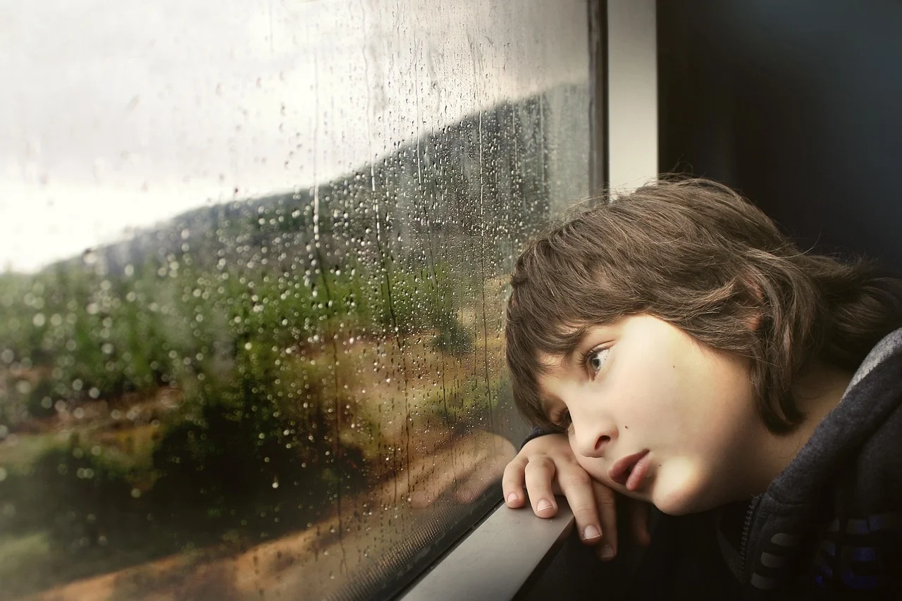 Kind sitzt am Zugfenster und schaut gelangweilt raus.